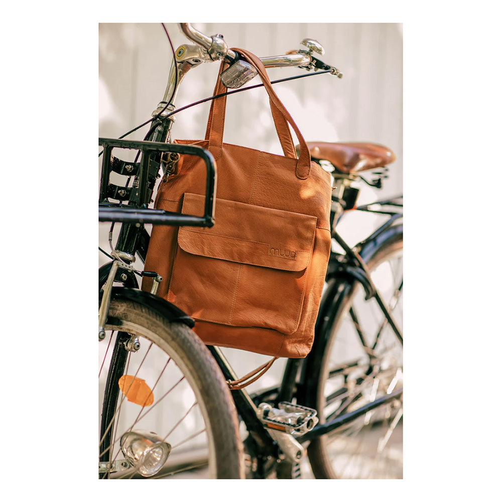 A brown leather knitting project bag with a zipper pocket and a front pocket with magnetic closure, displayed on a bicycle.