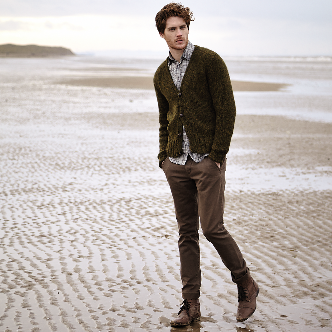 Man standing on a beach wearing a green Stour cardigan and brown pants.