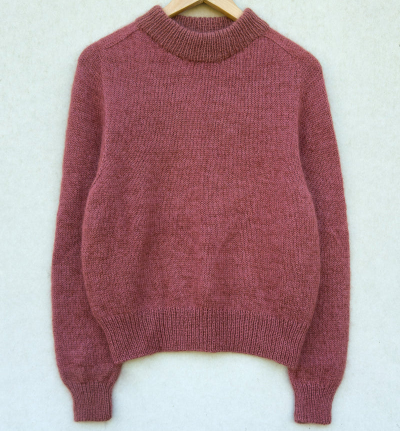 pink Knitting for Olive Carlie sweater on a wooden hanger against a light background