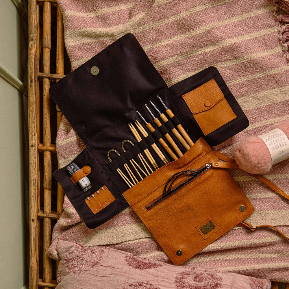 knitting needles and crochet hooks in a tan leather case from muud on a textured pink blanket
