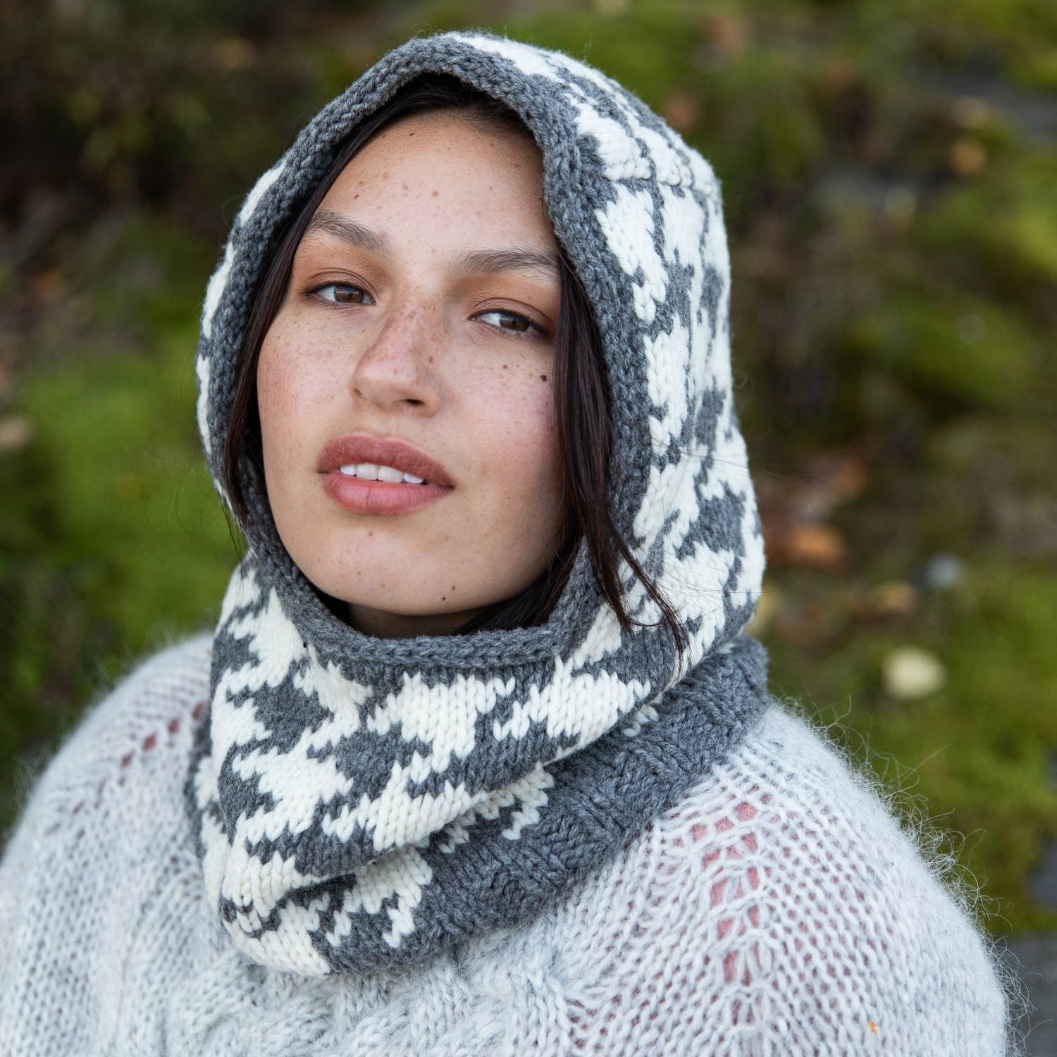 Woman wearing a patterned hood outdoors with greenery in the background