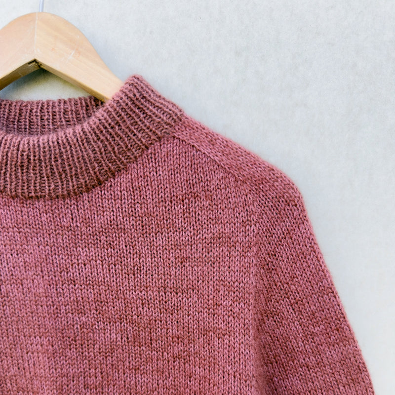 Pink Knitting for Olive Carlie sweater on a wooden hanger against a light background