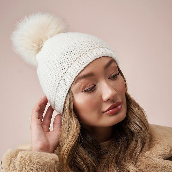 Woman wearing a white knit beanie with a pom-pom on a pink background