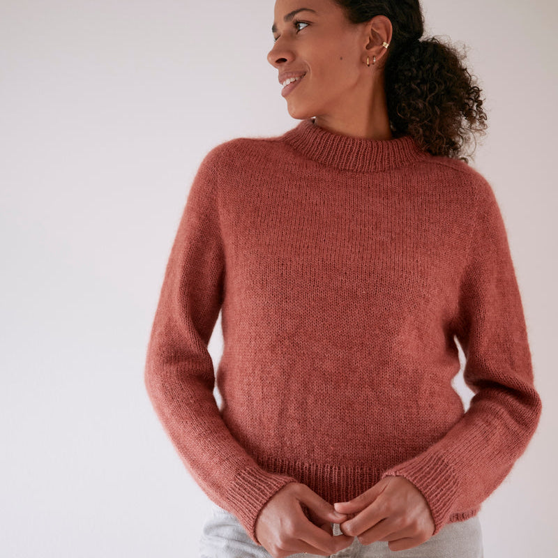 Woman wearing a pink handknitted Carlie Sweater by Knitting for Olive against a plain background