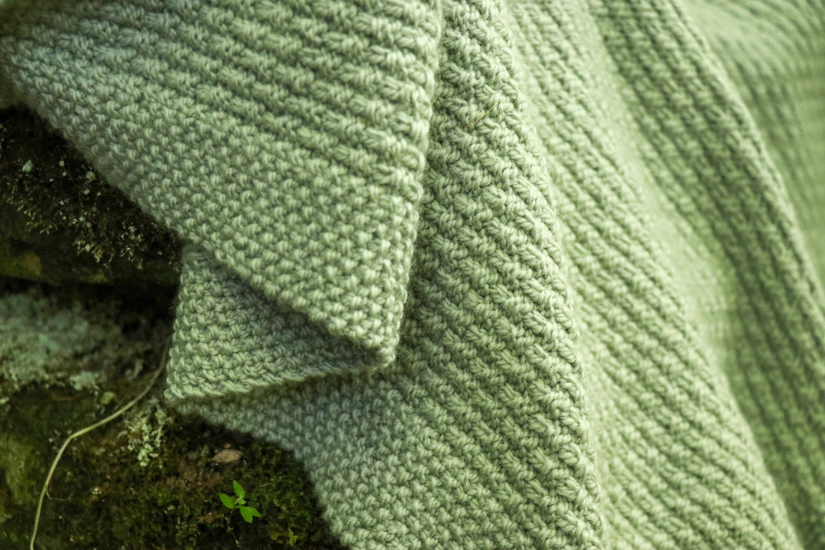 The Alloway Raindrops Baby Blanket folded, showing the moss stitch border