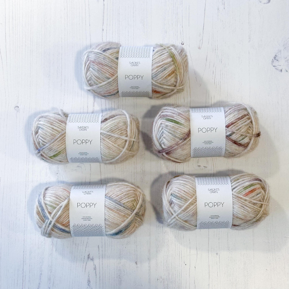 Five skeins of yarn labeled 'Poppy' on a light wooden surface