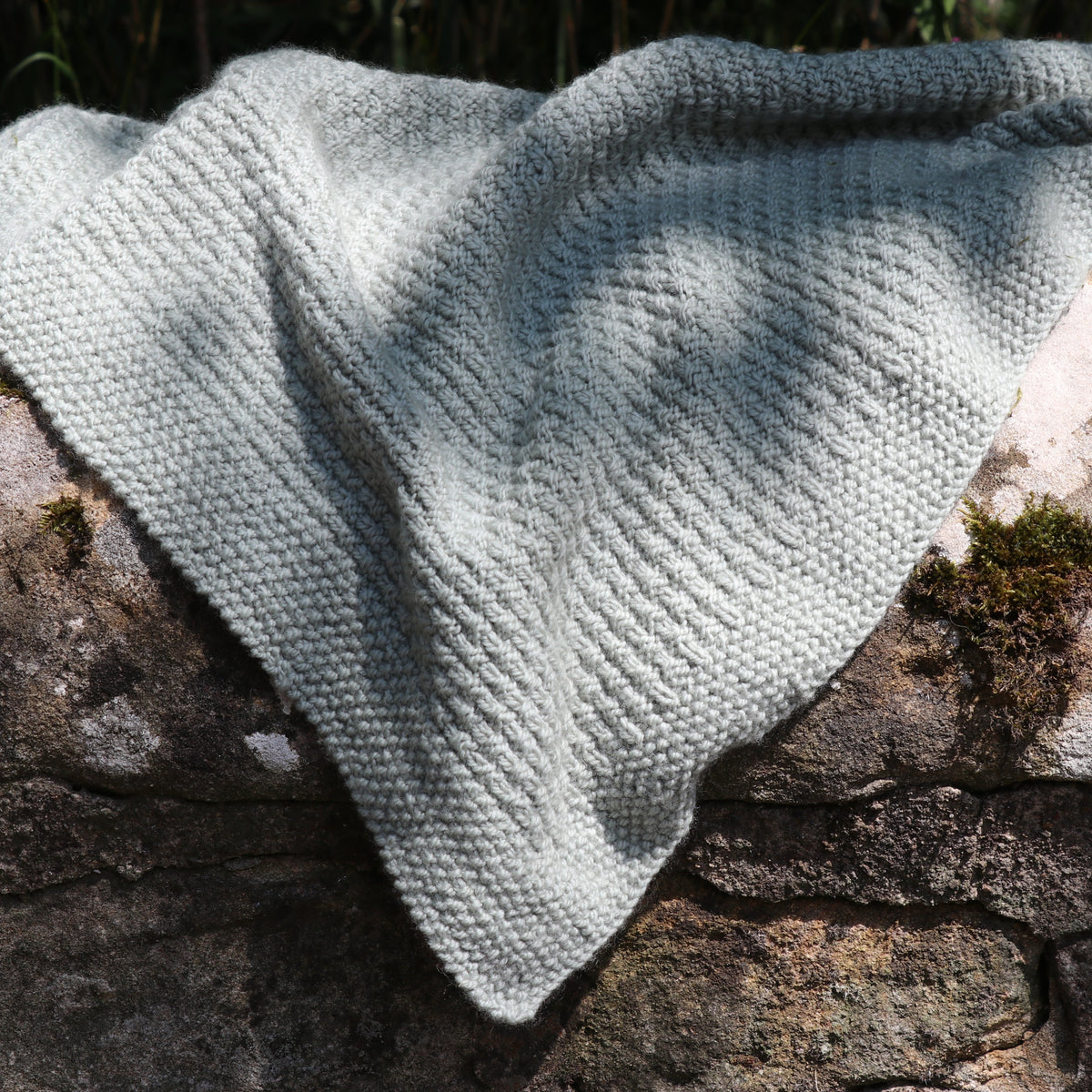 The Alloway Raindrops Baby Blanket knitted in Orry Yarn Merino DK, showing the raindrop texture and moss stitch edge