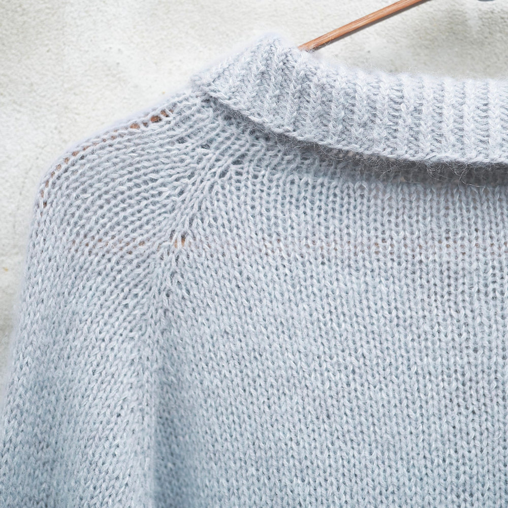 Detail of a pale blue Knitting for Olive Wilson Sweater on a hanger against a light background
