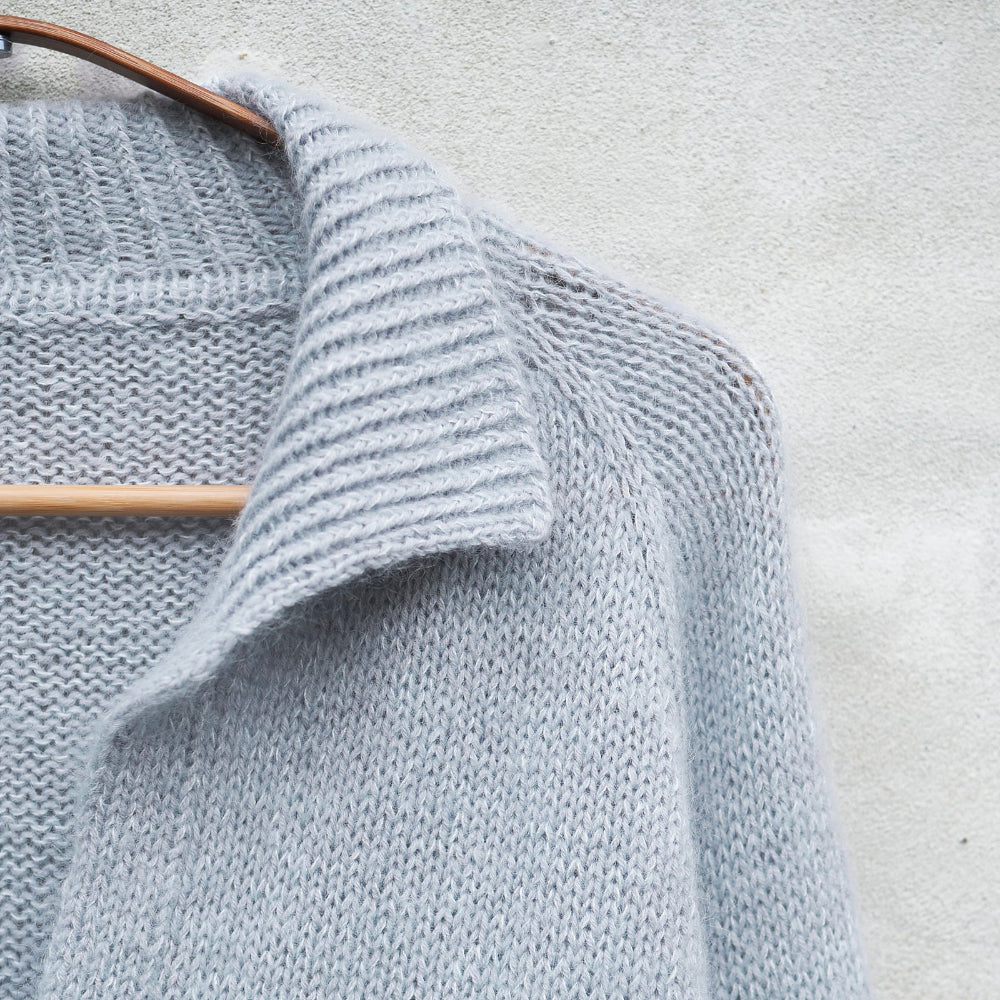 Front collar detail of a pale blue Knitting for Olive Wilson Sweater on a hanger against a light gray background