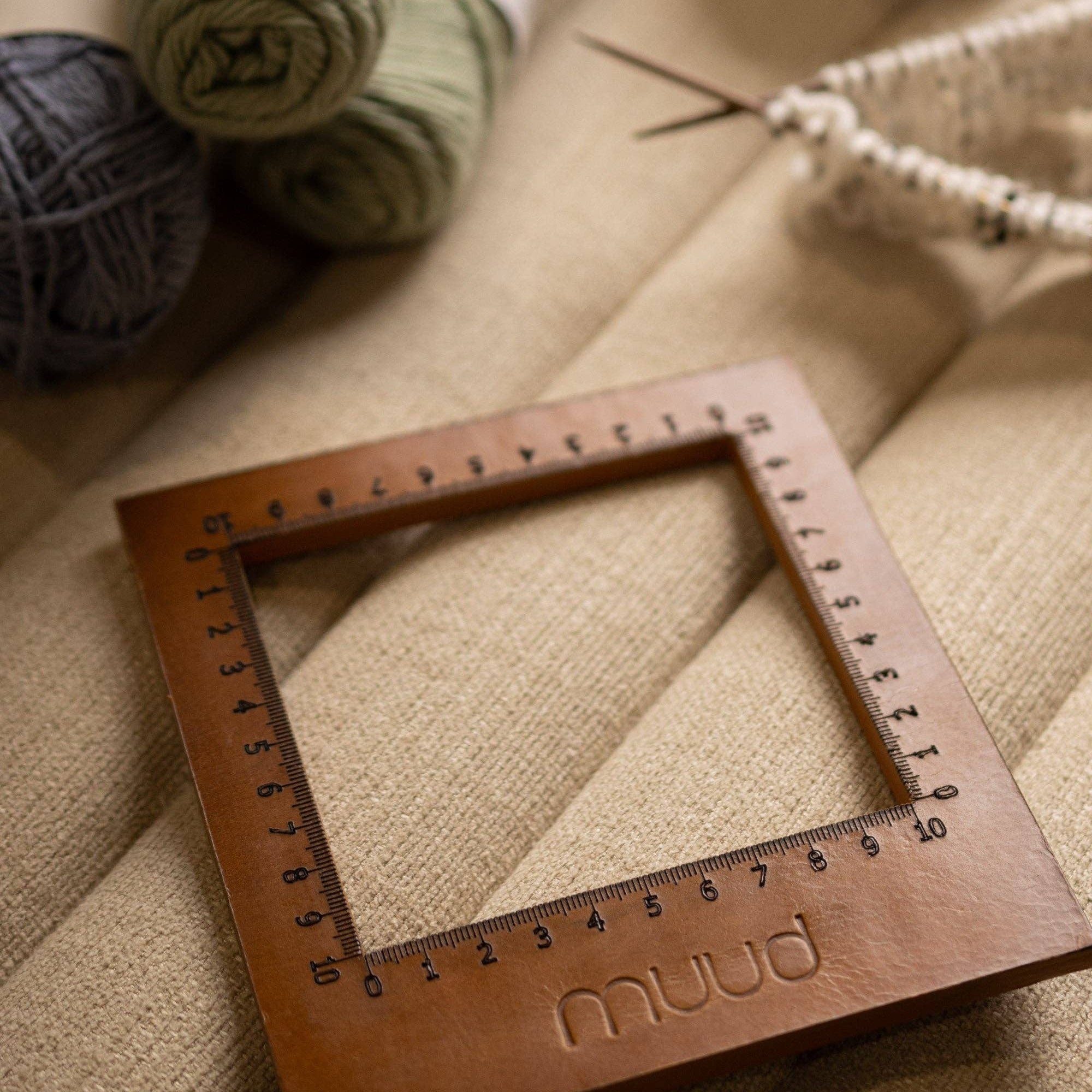 Leather knitting gauge by muud with ruler engraving on a textured surface, surrounded by yarn.