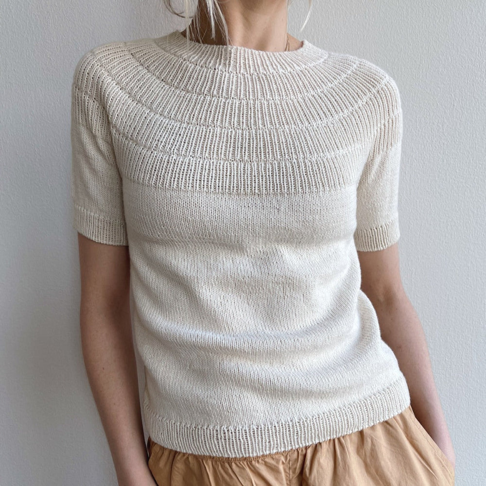 A person wearing an off white knitted Anker Tee by PetiteKnit. The top has short sleeves and a round neckline with a ribbed yoke.